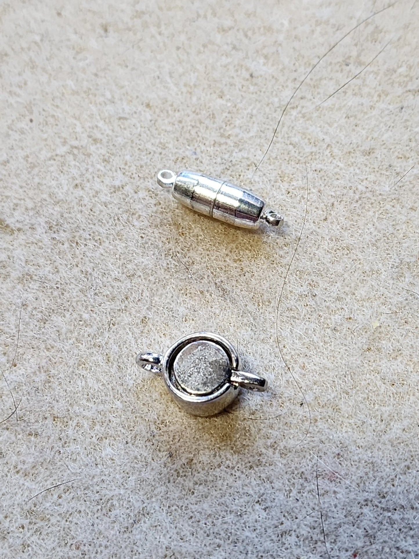 Sample of two silver tone magnetic clasps. One pulls apart, while the other has the two halves sit within each other.