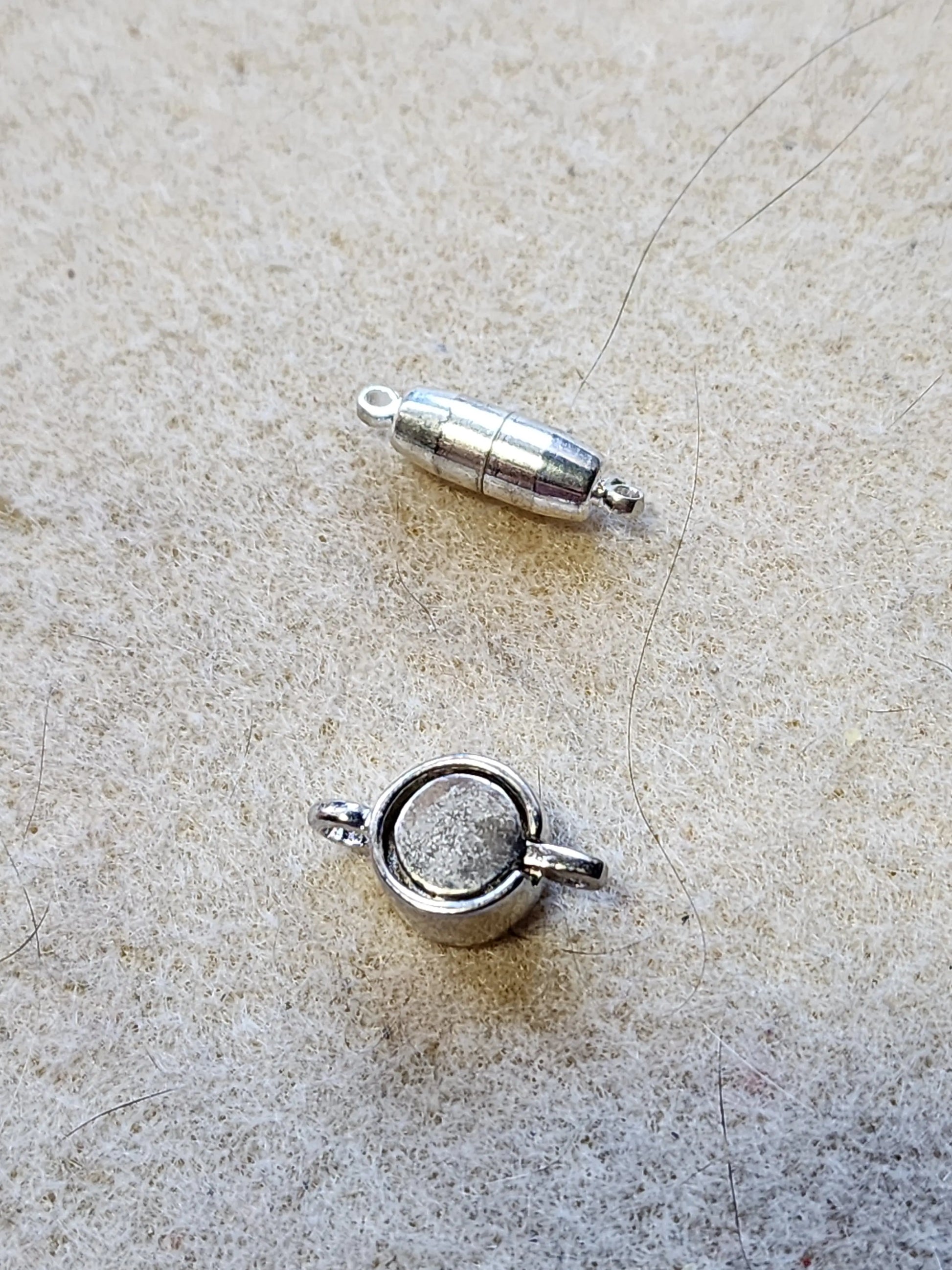 Sample of two silver tone magnetic clasps. One pulls apart, while the other has the two halves sit within each other.
